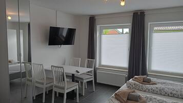 A modern room with a TV, white furniture, and a bed with patterned bedding.
