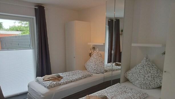 Een slaapkamer met twee eenpersoonsbedden, een grote spiegel, een kledingkast en een glazen schuifdeur naar buiten.