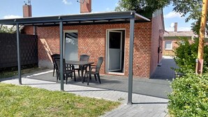 Een overdekt terras met een bakstenen muur, een deur en een tafel met stoelen.