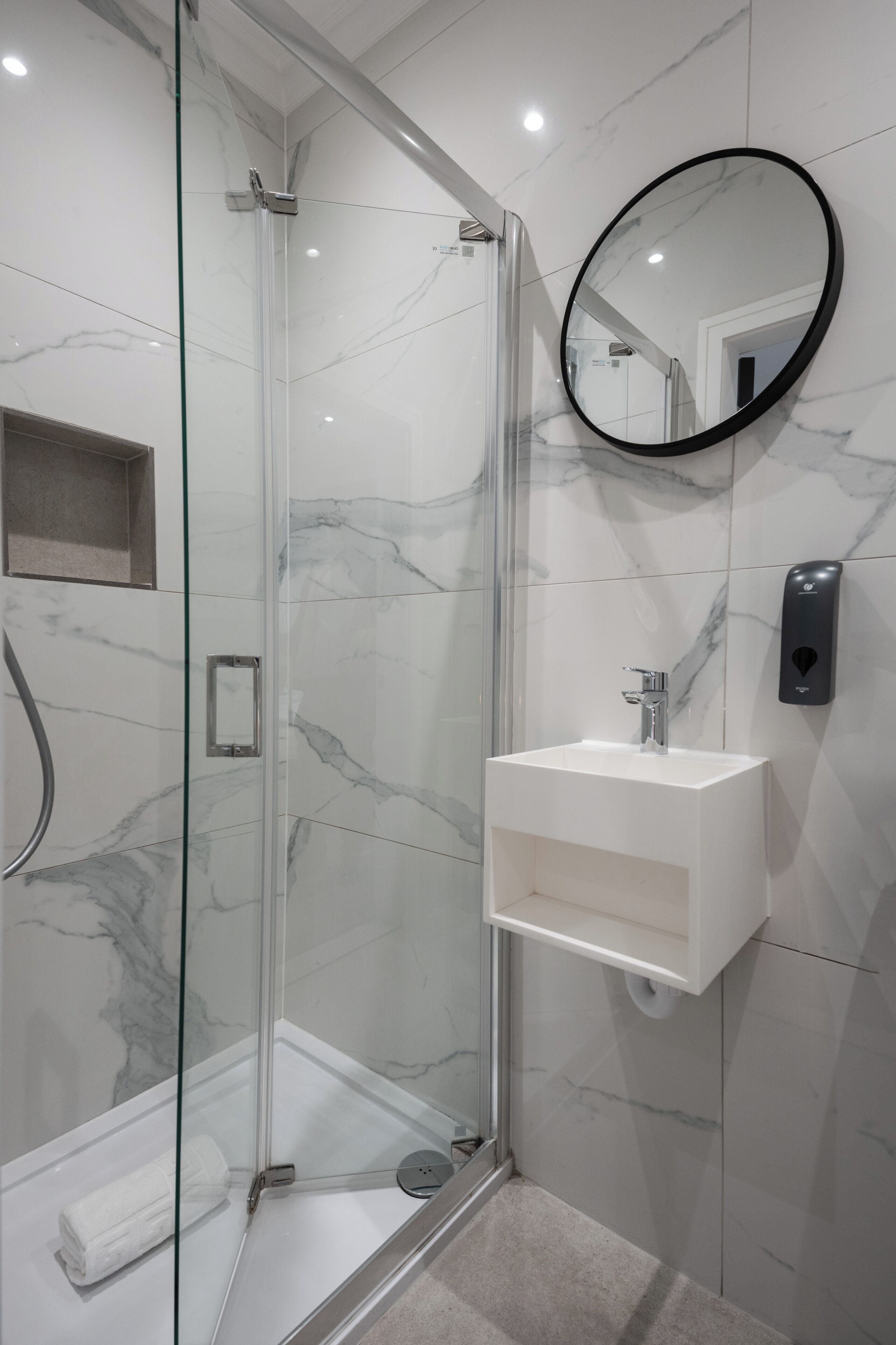 A modern bathroom with a glass shower enclosure, a white sink, and a marble-tiled wall.