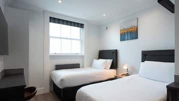 A hotel room with two beds, a desk, a chair, a window, and a painting on the wall.