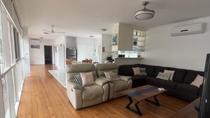 A spacious living room with a wooden floor, a beige sofa set, a dark-colored couch, and a wooden coffee table. - Classic beach Getaway - Close to winery region and beach! (Dromana)