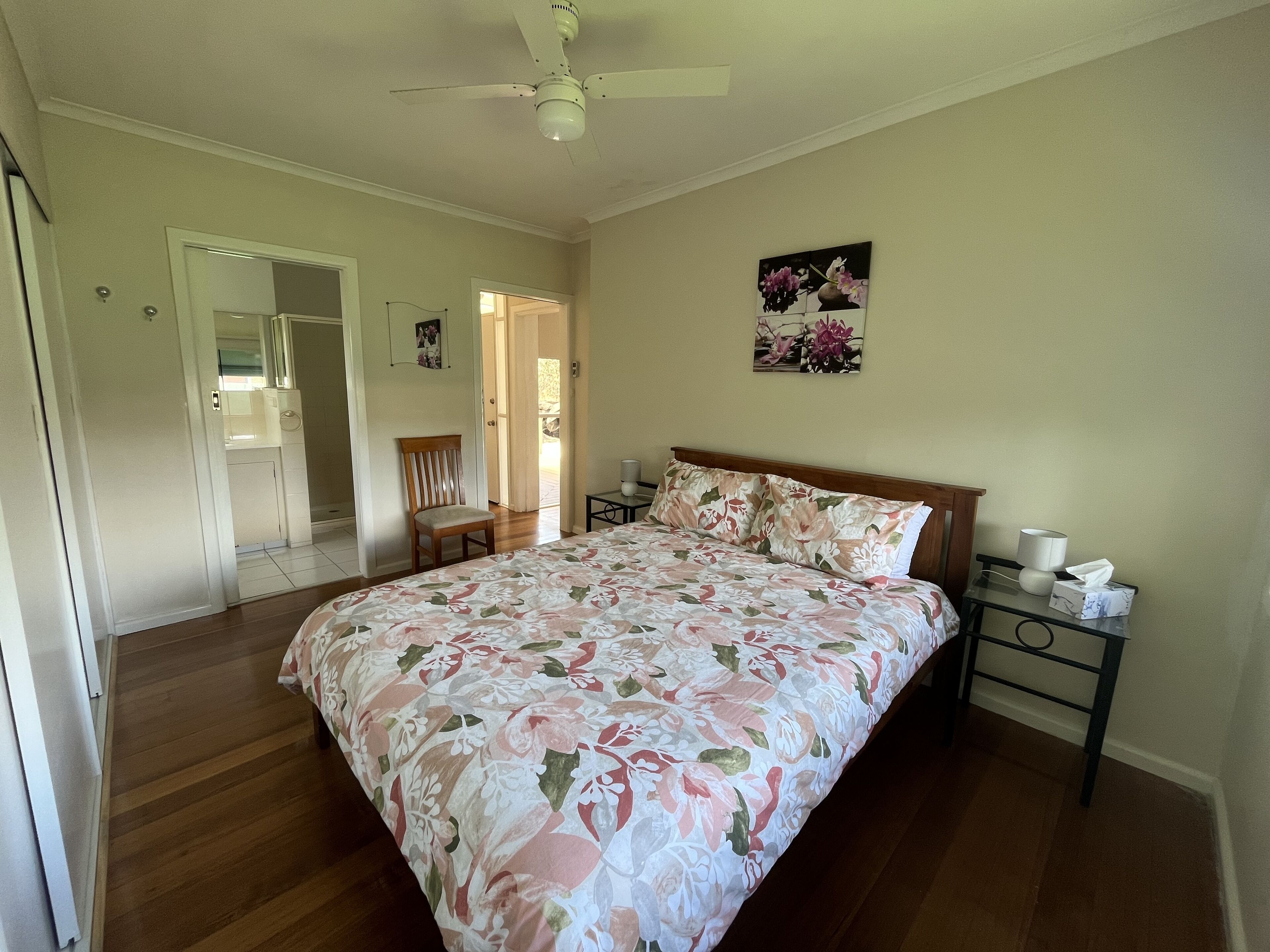 A bedroom with a floral bedspread, a wooden headboard, a nightstand with a lamp, and a door leading to another room.