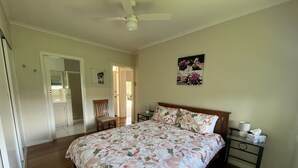 A bedroom with a floral bedspread, a wooden headboard, a nightstand with a lamp, and a door leading to another room. - Classic beach Getaway - Close to winery region and beach! (Dromana)