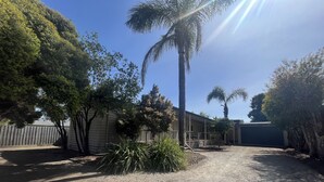 A residential area with a gravel driveway, a wooden fence, and a house with a covered patio. - Classic beach Getaway - Close to winery region and beach! (Dromana)