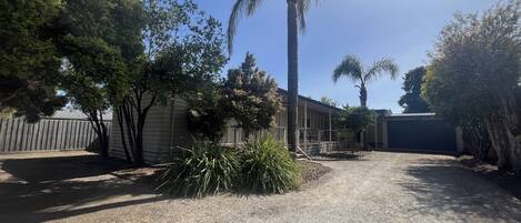 A residential area with a gravel driveway, a wooden fence, and a house with a covered patio.