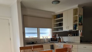 A dining area with a table and chairs, a kitchen with cabinets and appliances, and a view of the sea through a window. - Classic beach Getaway - Close to winery region and beach! (Dromana)