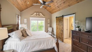Une chambre avec un plafond en bois, un lit avec une literie blanche, une table de chevet, une commode et un téléviseur.
