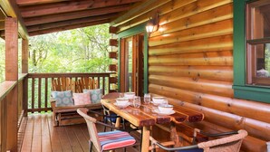 A wooden cabin with a covered porch, a dining table set with white plates and glasses, and a bench with cushions.