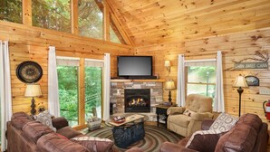 A cozy cabin interior with a stone fireplace, leather sofas, and a television.