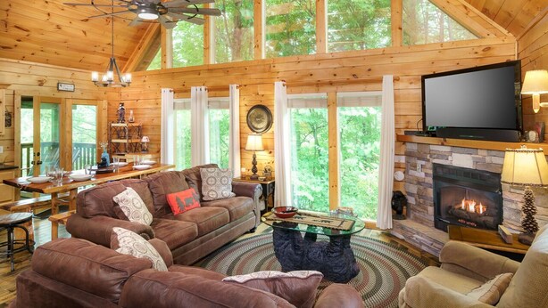 A spacious cabin interior with a large wooden ceiling, a fireplace, a television, and a dining area with a table and chairs.