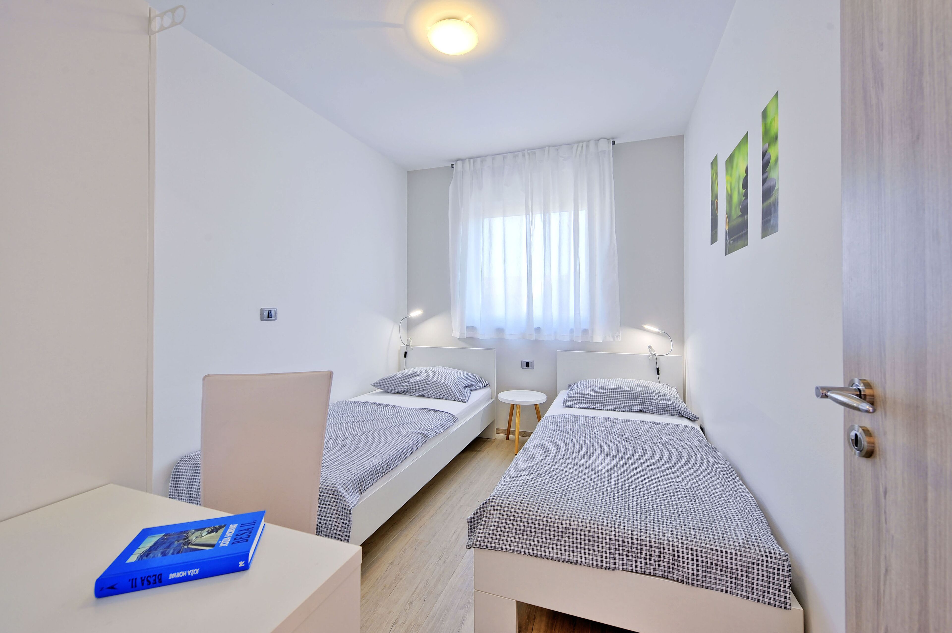 A small, well-lit room with two single beds, a small table, and a door.
