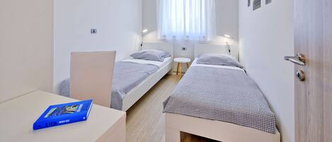 A small, well-lit room with two single beds, a small table, and a door.