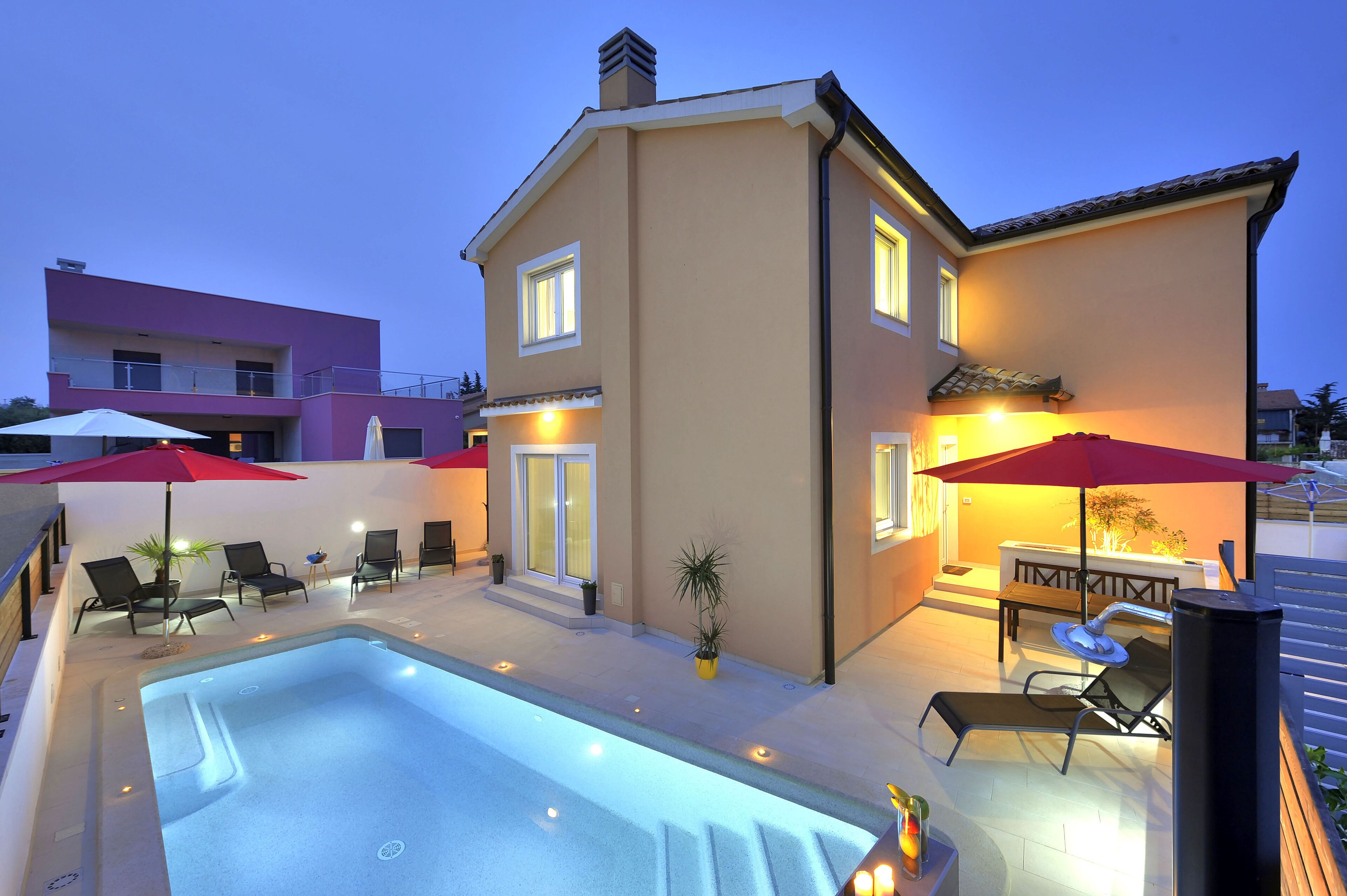 A modern house with a swimming pool, outdoor seating, and a well-lit patio area.