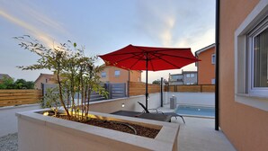 A rooftop patio with a red umbrella, a pool, and a planter with plants.