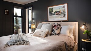 A bedroom with a large bed, multiple pillows, a framed picture on the wall, and a window with a view of trees.