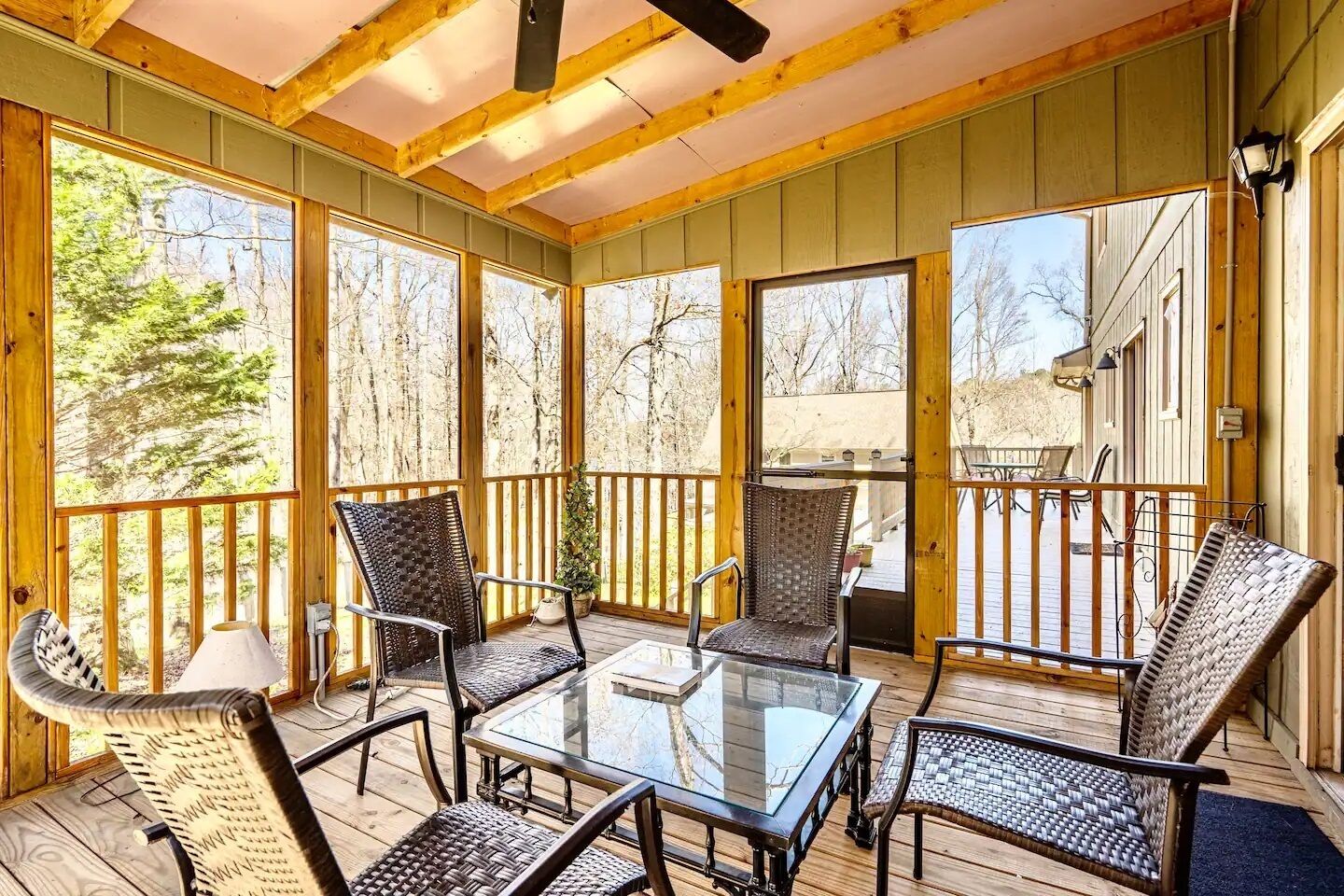 A covered outdoor area with a glass table and wicker chairs, wooden beams, and large windows.