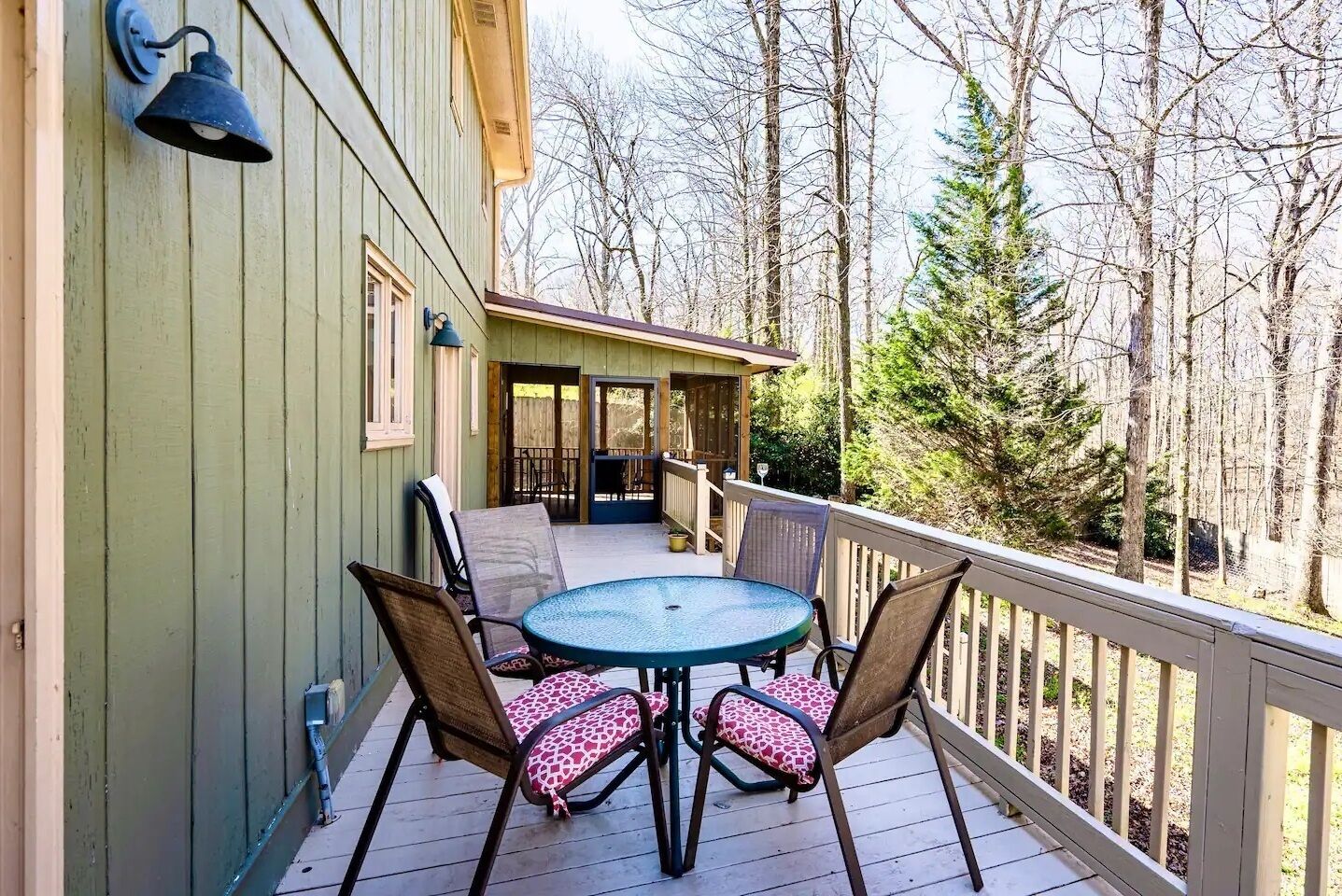 A wooden deck with a round table and four chairs, a covered patio area, and a view of a forested area.