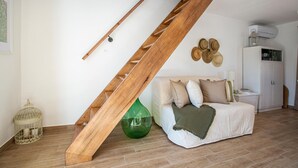 Une pièce avec un escalier en bois, un vase en verre vert, un canapé blanc avec des coussins, une armoire blanche et un porte-chapeaux fixé au mur.