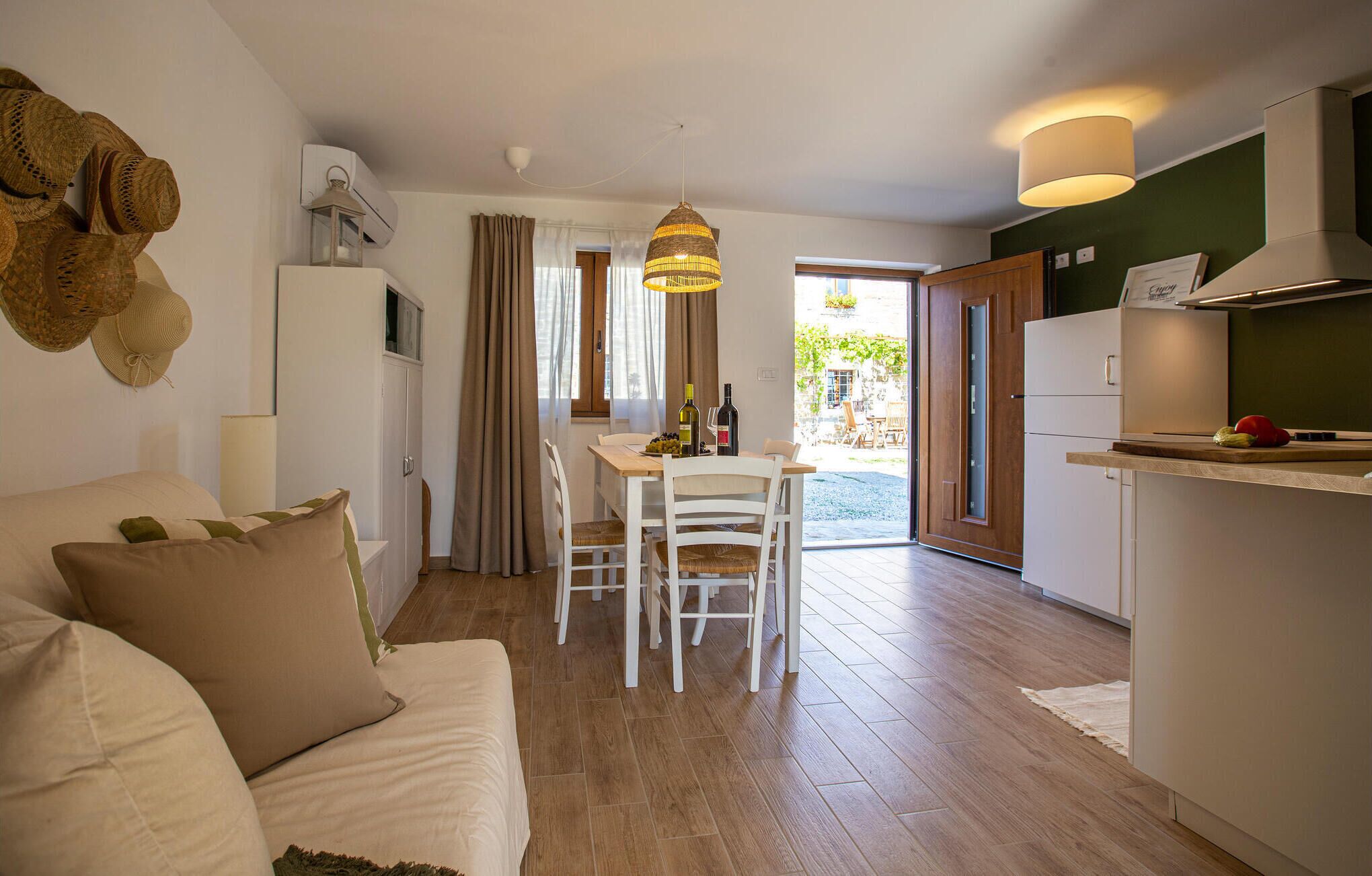 Un salon confortable avec un canapé, une table à manger et des chaises, un coin cuisine équipé d’un réfrigérateur et d’une cuisinière, et une vue sur l’extérieur grâce à une porte vitrée.