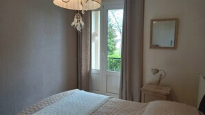 Een slaapkamer met een bed, nachtkastje, spiegel en raam met gordijnen.