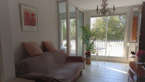 Een woonkamer met een bank, een potplant, een kroonluchter en uitzicht door grote ramen.
