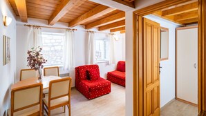A room with a wooden ceiling, a dining table with chairs, a red sofa, and a door. - Apartment Ribambit (Dubrovnik)