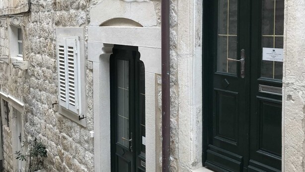 A stone building with two black doors and a small window with shutters. - Apartment Ribambit (Dubrovnik)