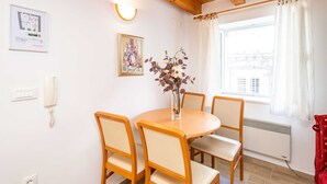 A dining area with a round table and four chairs, a framed painting on the wall, a telephone, and a window with curtains. - Apartment Ribambit (Dubrovnik)