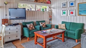 Ein Wohnzimmer mit einem grünen Sofagarnitur, einem Holztisch, einem Flachbildfernseher und einem Bücherregal.