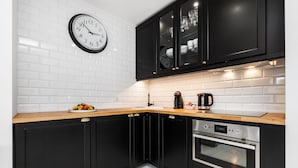 A modern kitchen with black cabinets, a wooden countertop, a stainless steel oven, and a white brick backsplash.