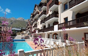 A hotel with multiple balconies, a swimming pool, and mountain views.