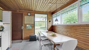 A cozy cabin interior with a wooden interior, a dining table with chairs, a kitchen area with a kettle, and a view of greenery outside. - Amazing home in Nykøbing M (Nykøbing M)