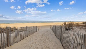 A sandy beach path leading to the ocean, bordered by wooden fences.