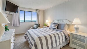 A bedroom with a bed, bedside tables, a TV, and a window with curtains.