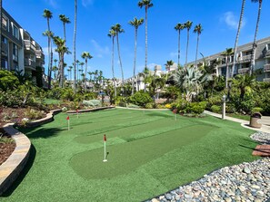 A golf course with a putting green surrounded by palm trees and a pool area.