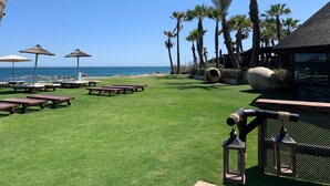 Een terras aan het strand met rieten parasols, houten tafels en uitzicht op de oceaan.
