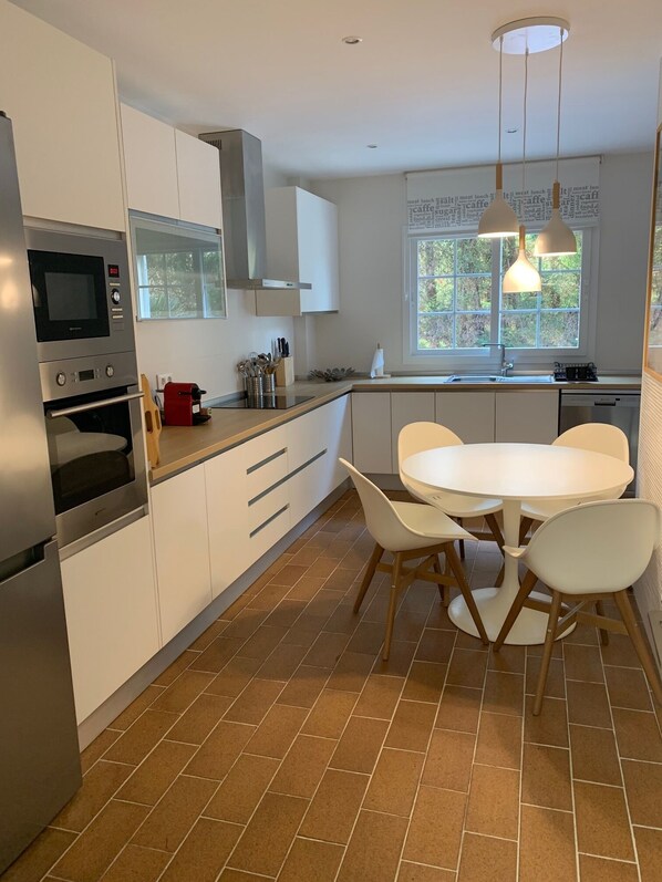A modern kitchen with white cabinets, a built-in oven, a microwave, and a dining area with a round table and chairs.