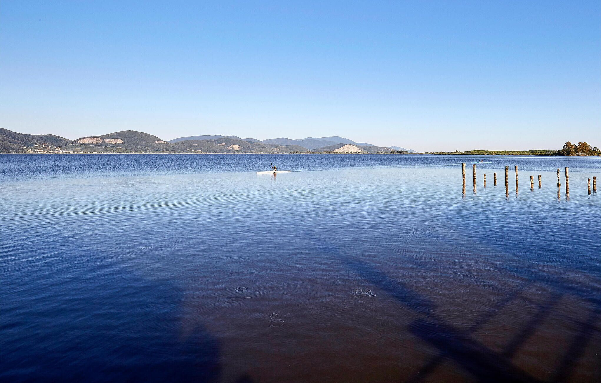 A calm lake with clear water, surrounded by hills and a distant shoreline.