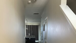 Um corredor estreito com piso de madeira, um tapete e uma área de cozinha ao fundo, com pia e armários.