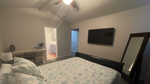 Quarto com uma cama, uma escrivaninha, uma cadeira, uma televisão e um espelho.