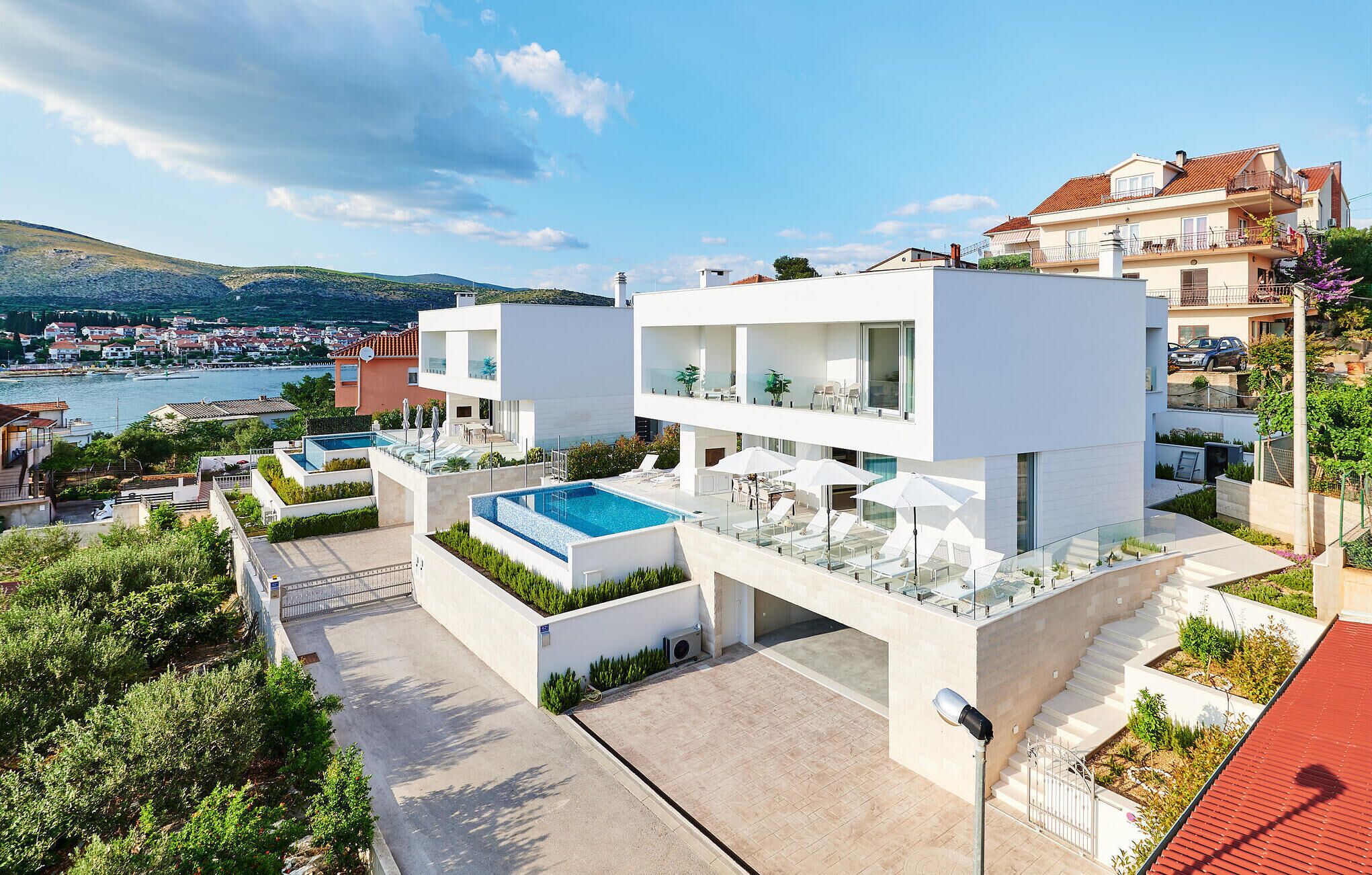 Ein modernes, zweistöckiges Gebäude mit Pool auf dem Dach, einer überdachten Terrasse und Blick auf das Meer und die Stadt.