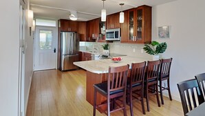 A modern kitchen with wooden cabinets, stainless steel appliances, and a central island with bar stools. - Luxurious Kihei Remodeled 2BR Condo Sweeping Ocean Views Near Keawakapu (Kihei)