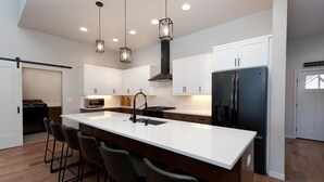 A modern kitchen with white cabinetry, a large island with bar stools, stainless steel appliances, and pendant lighting.