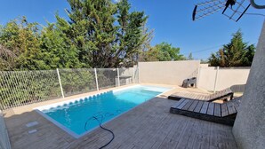 Ein Schwimmbecken mit Holzterrasse, umgeben von einem weißen Zaun und Bäumen.