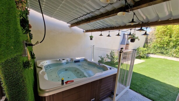 Ein Whirlpool mit Holzverkleidung, umgeben von einem weißen Zaun, mit einem Rasen im Hintergrund.