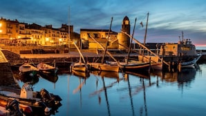 Un port où sont amarrés des bateaux, un bâtiment historique doté d’une tour et un ciel au coucher du soleil.