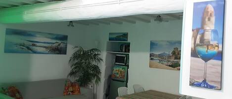 A room with a green sofa, a small table, a potted plant, and artwork on the walls.