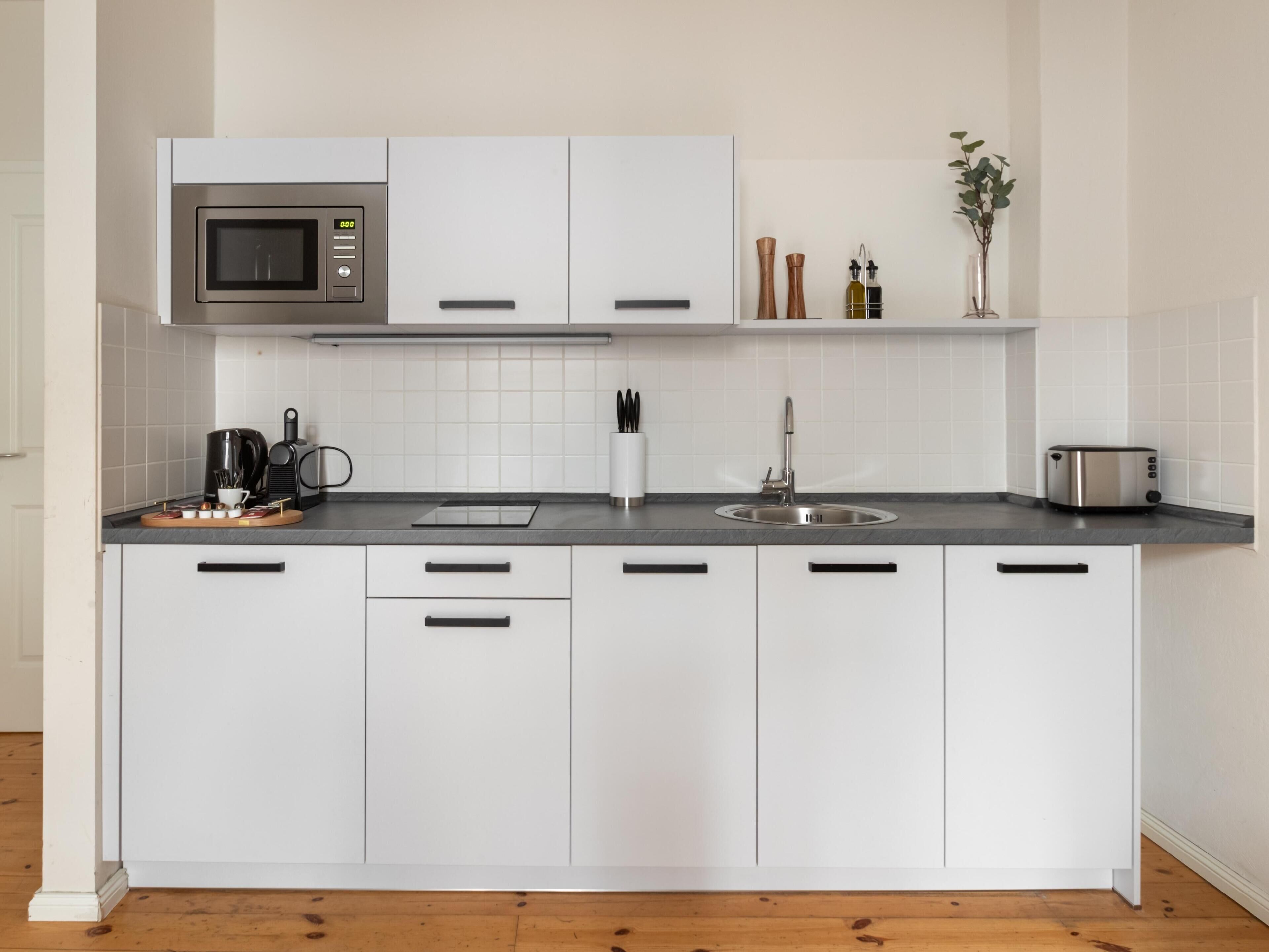 A modern kitchen with white cabinets, a stainless steel microwave, a toaster, and a coffee maker.