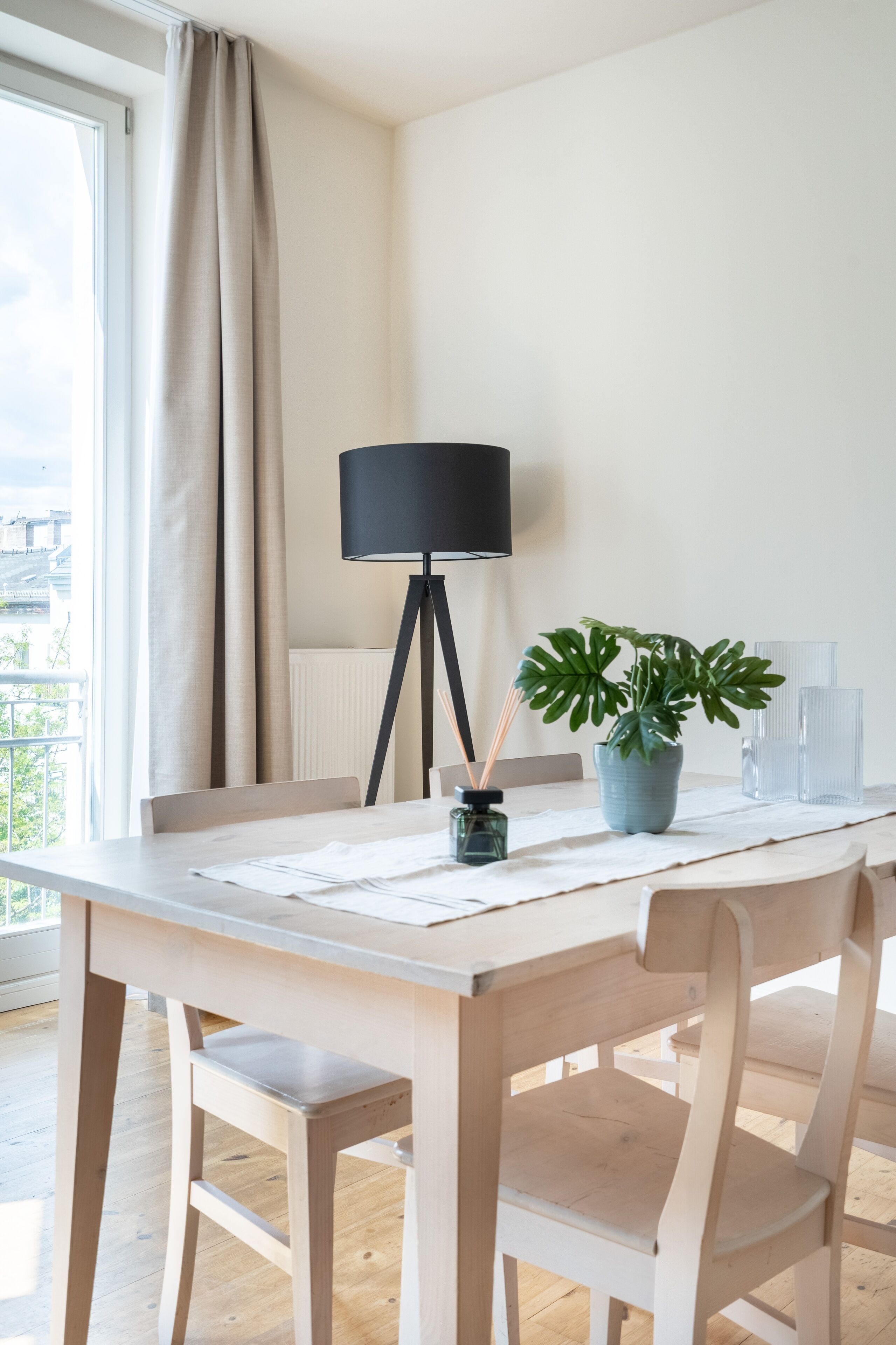 Une pièce moderne avec une table à manger en bois, une plante en pot, une lampe et une vue sur l’extérieur.